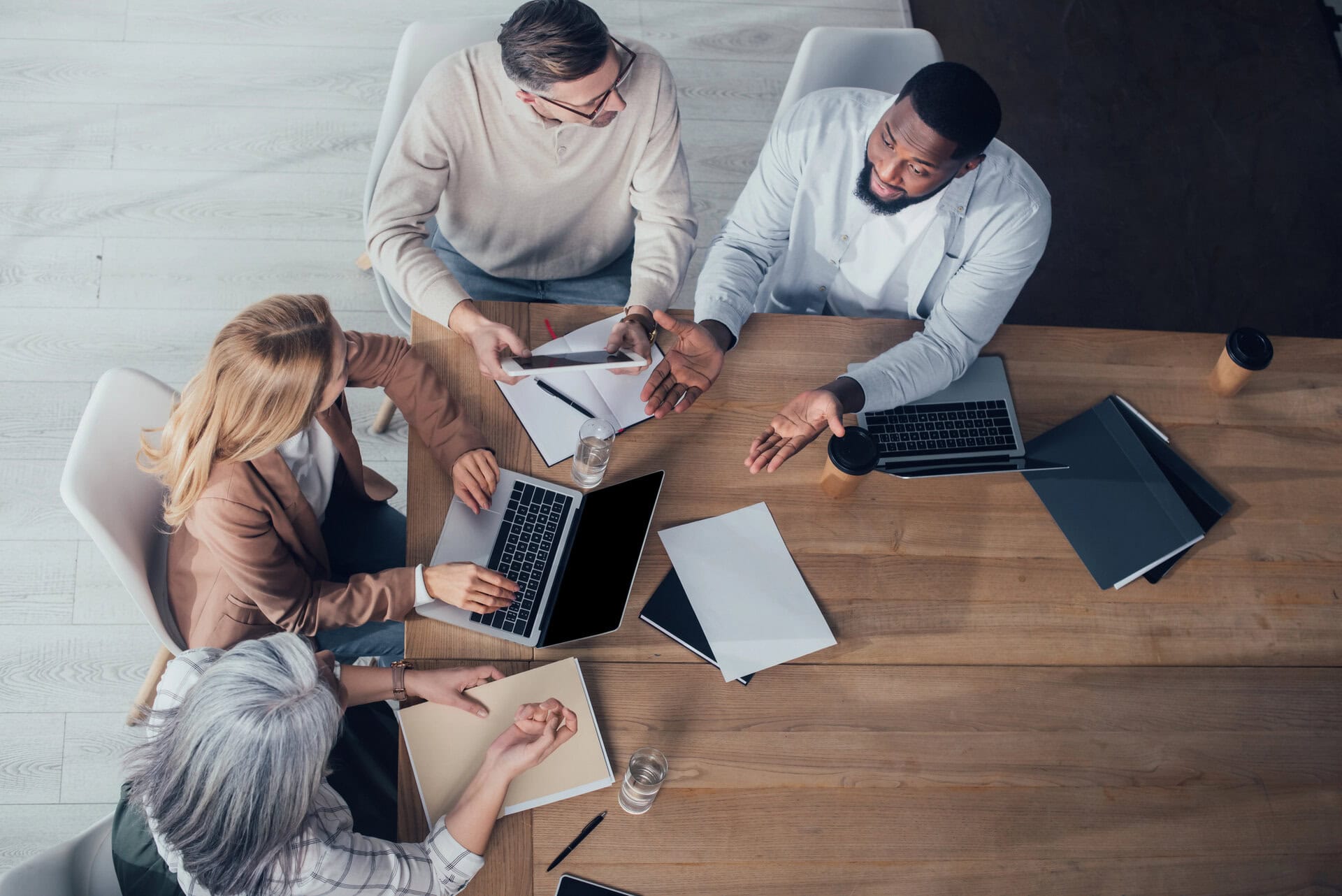 Overhead view of multicultural colleagues talking and sitting at table during meeting