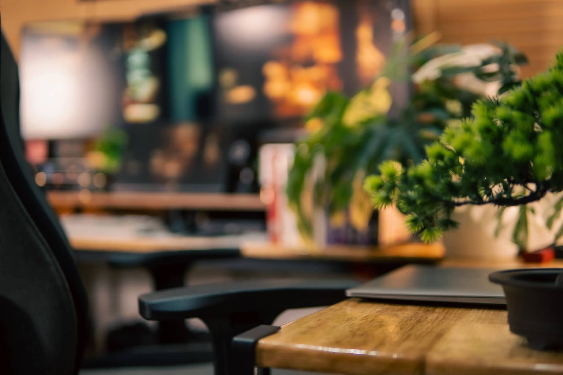 A warm and cozy desk setup featuring triple monitors, notebook, microphone, and green plants, styled in a minimalist Japanese aesthetic for creative work